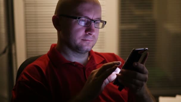 Hombre con gafas sentado en una oficina usando un smartphone — Vídeos de Stock