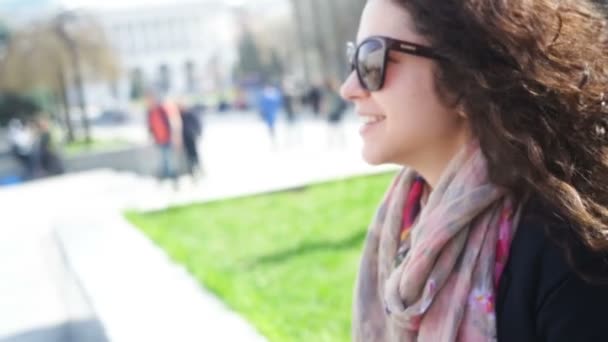 Heureuse jeune femme en lunettes s'assoit sur un banc dans la ville — Video