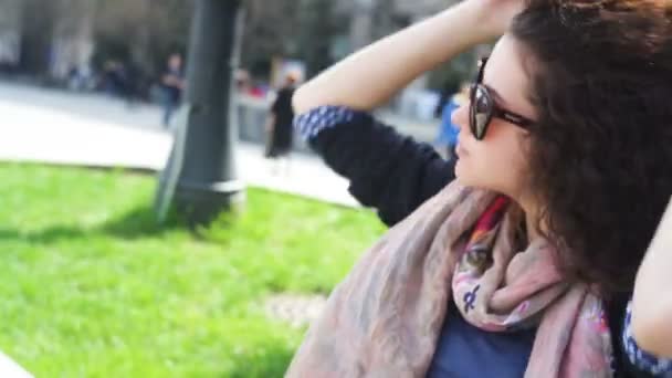 Felice giovane donna in occhiali si siede su una panchina in città — Video Stock