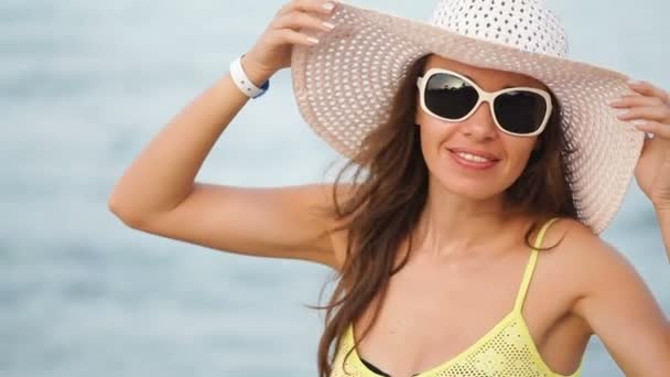 Mujer joven en gafas y un sombrero en una playa cerca del mar — Vídeo de stock