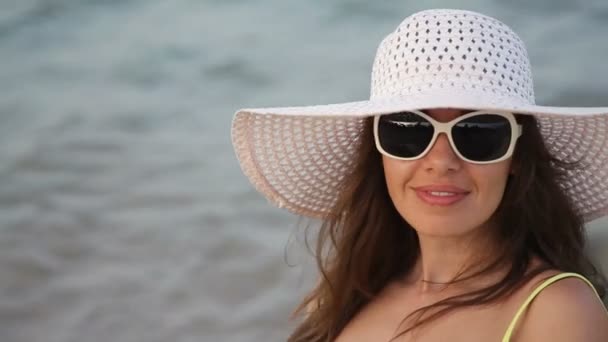 Giovane donna in occhiali e un cappello su una spiaggia vicino al mare — Video Stock