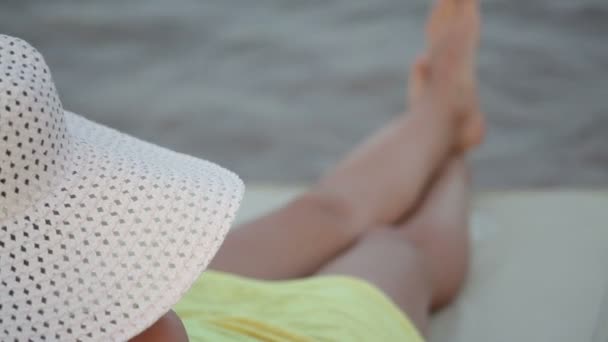 Hermosa mujer con sombrero tumbona para tomar el sol en la playa — Vídeo de stock