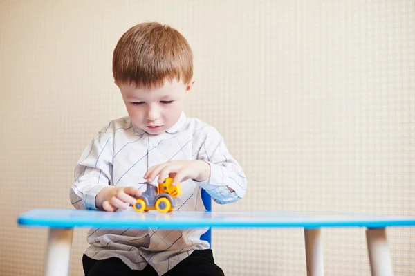 Mały chłopiec bawi się kolorowe zabawki samochodu na stole — Zdjęcie stockowe
