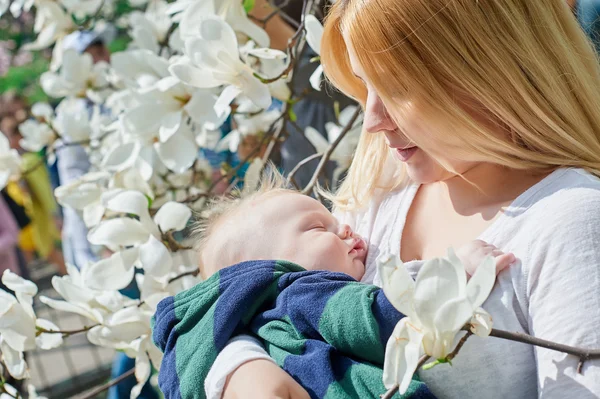 Matka se synem dítě sedící na větvi stromu v jarní zahradě — Stock fotografie