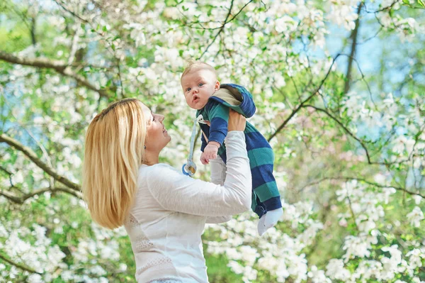 Pequeño niño con madre joven en el jardín de flores de primavera —  Fotos de Stock