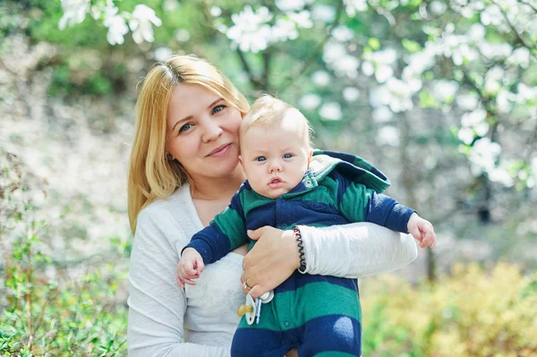 Mãe andando com seu filho bebê no jardim de magnólias florescendo — Fotografia de Stock