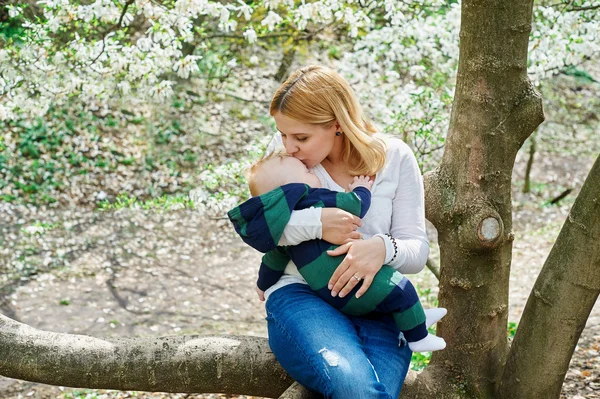 Mamma med hennes baby son sitter på trädgren i vårträdgård — Stockfoto