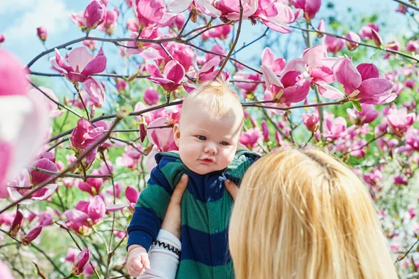 Mamma går med sin baby son i trädgården av blommande magnolior — Stockfoto