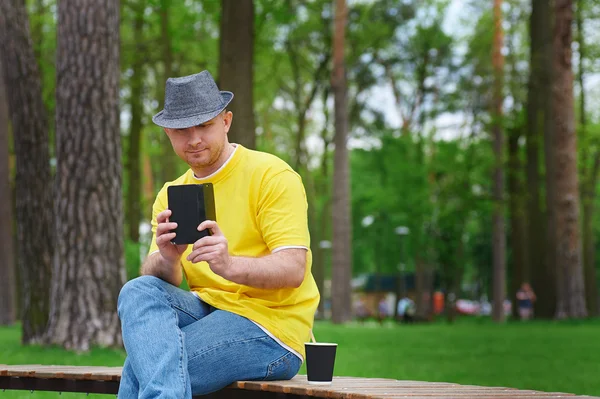 man sits on bench in park with smartphone