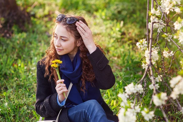 花の咲く春の庭で歩いて黒いコートの若い女性 — ストック写真