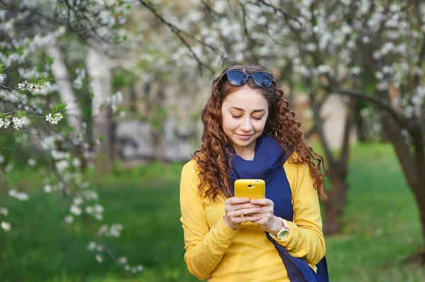 Mujer joven en el floreciente jardín de primavera con teléfono inteligente — Foto de Stock