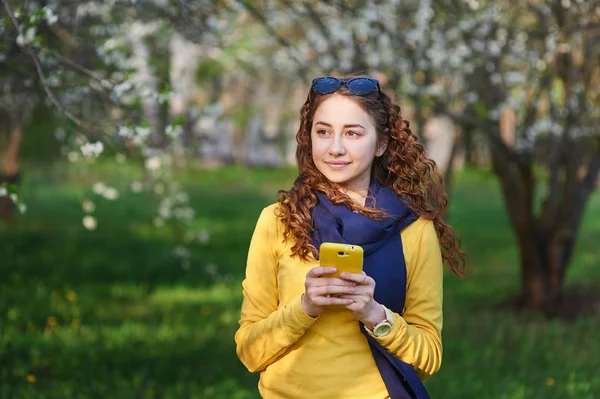 Mujer joven en el floreciente jardín de primavera con teléfono inteligente — Foto de Stock