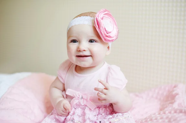 Schattige mooie babymeisje zittend op een bed in roze jurk en glimlachen — Stockfoto