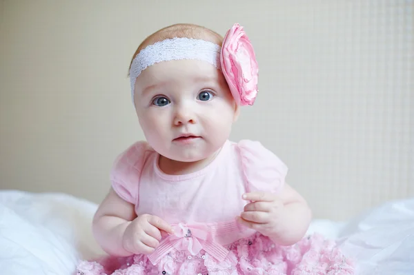 Schattige mooie babymeisje zittend op een bed in roze jurk — Stockfoto