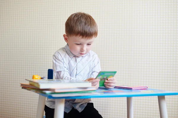 Little boy sitting at the desk and reading a book — Stock Photo, Image