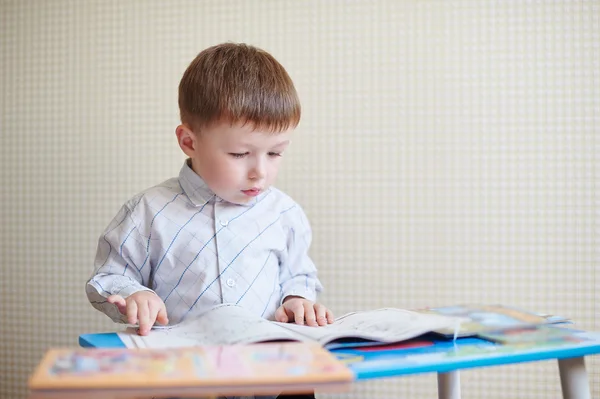 小男孩坐在桌前，读一本书 — 图库照片