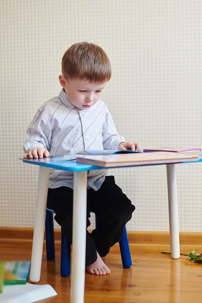 Kleiner Junge sitzt am Schreibtisch und liest ein Buch — Stockfoto