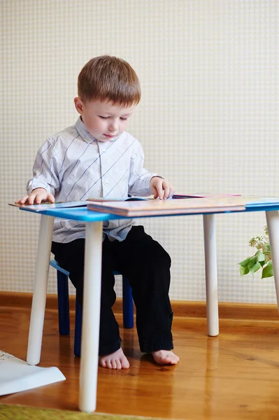 Mały chłopiec siedzi przy biurku i czytanie książek — Zdjęcie stockowe