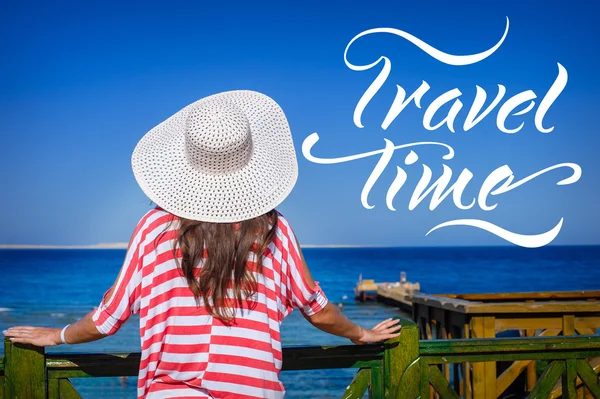 Una mujer con un gran sombrero blanco mira al mar. palabras Tiempo de viaje — Foto de Stock