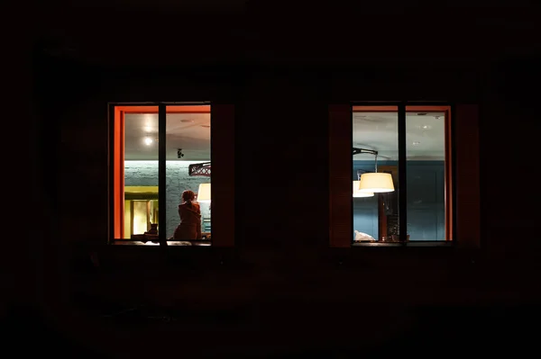 Frau sitzt nachts in einem beleuchteten Zimmer in der Nähe des Fensters — Stockfoto