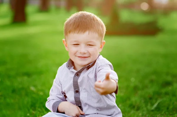 Menino sorridente senta-se na grama verde no parque de verão — Fotografia de Stock