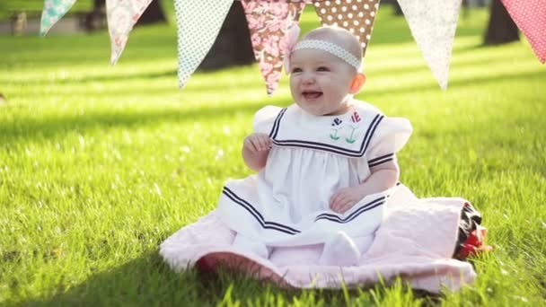Søt liten jente som sitter på gresset på en solrik sommerdag – stockvideo