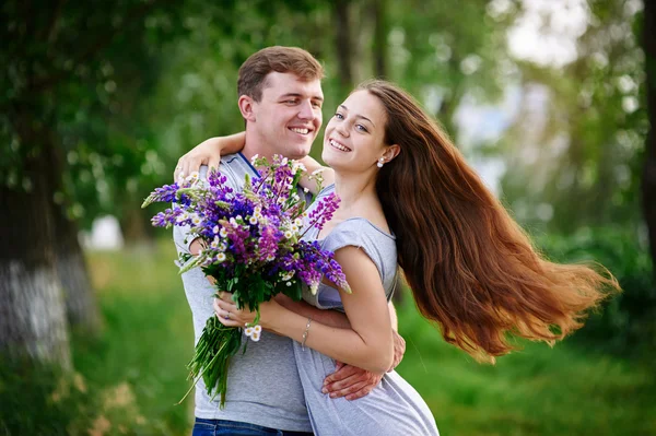 Beautiful woman with long hair and a happy man hugging in field — Stock Photo, Image