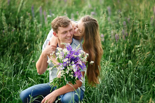 Piękna kobieta z bukietem kwiatów dzikiego przytulanie człowiek siedzi na trawie w łące — Zdjęcie stockowe