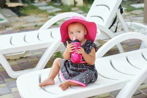 Bambina in cappello rosso siede su un lettino — Foto Stock