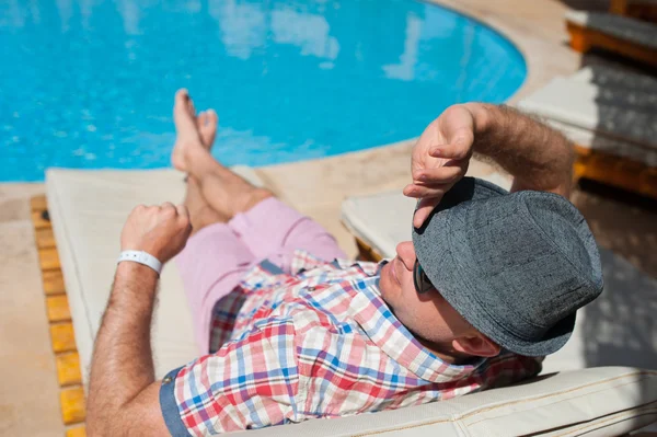 Homme au chapeau allongé sur une chaise longue au bord de la piscine — Photo