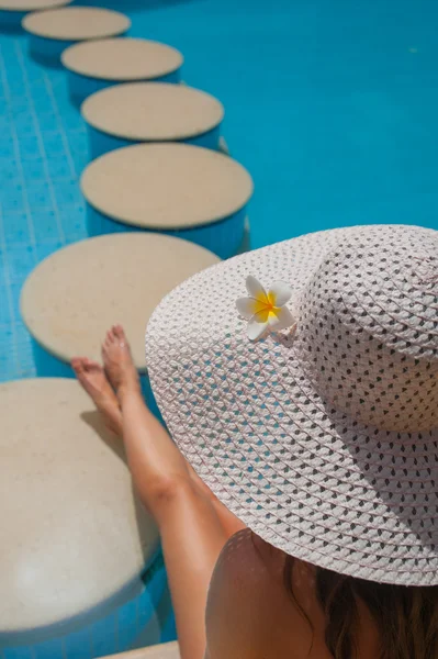Vrouw in een grote witte hoed zit op de rand van het zwembad met stenen — Stockfoto