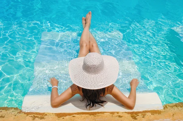 Mulher de chapéu grande deitada na espreguiçadeira junto à piscina — Fotografia de Stock