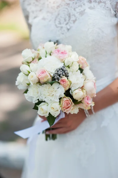 Букет свадебных цветов в руках невесты с белым платьем на заднем плане — стоковое фото