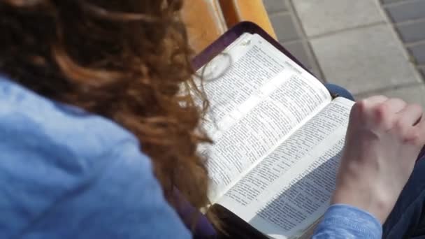 Mulher sentada em um banco no parque e lendo livros da Bíblia — Vídeo de Stock