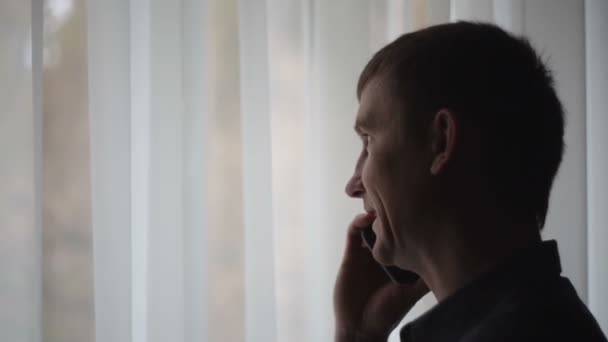 Zakenman kijkt uit het raam en praten over de telefoon — Stockvideo