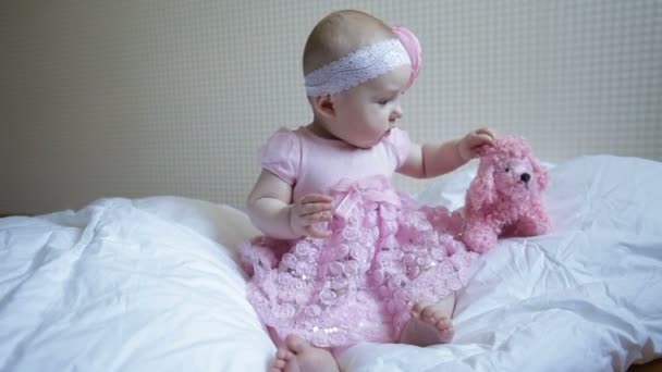 Schattige mooie babymeisje zittend op een bed in roze jurk — Stockvideo