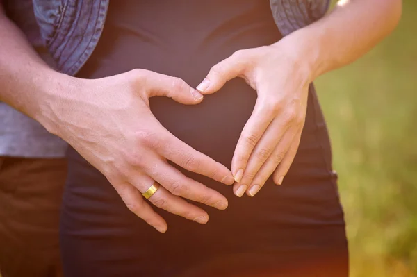 Pancia incinta con le dita del marito Simbolo del cuore — Foto Stock