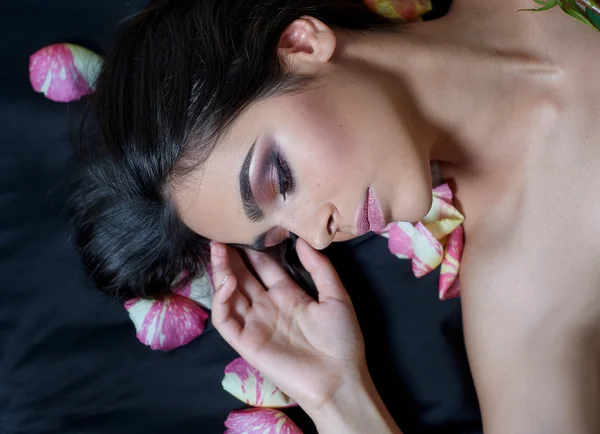 Retrato de uma bela jovem que coloca em pétalas de rosa esparsas — Fotografia de Stock