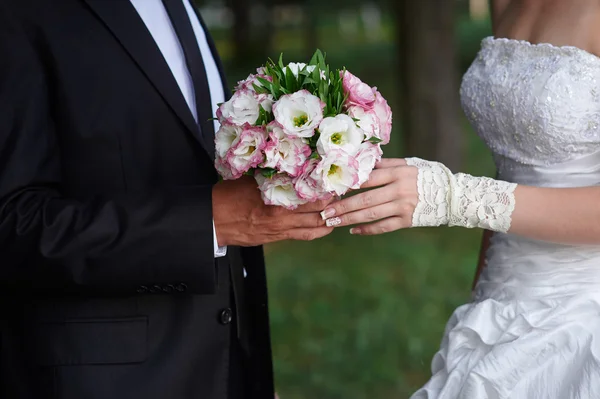 Groom embraces bride, and she holds a bridal bouquet in his hands — Stock Photo, Image