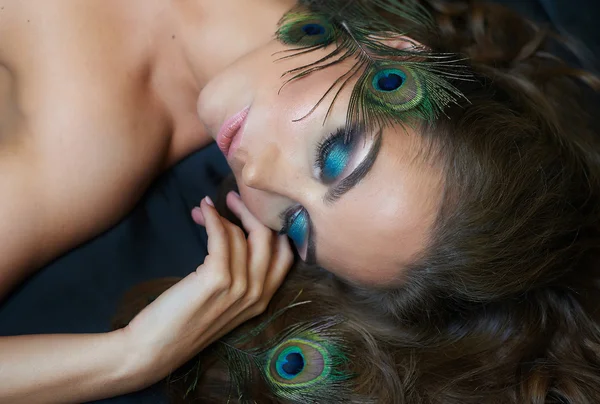 Красивая женщина лежит на кровати с павлиньим пером и макияжем — стоковое фото