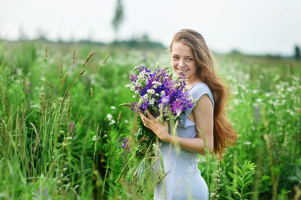 Jovem mulher bonita com um buquê de flores no prado de verão — Fotografia de Stock