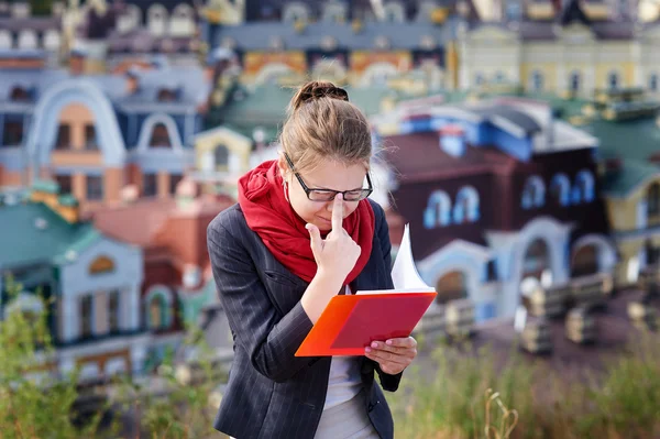 手の中都市の背景に赤いフォルダーとメガネの若い女性 — ストック写真