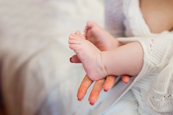 Madre sosteniendo pequeños pies de bebé en la cama —  Fotos de Stock