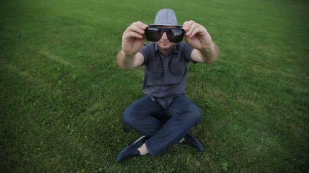 Man in the hat wears sunglasses sitting on the grass — Stock Video