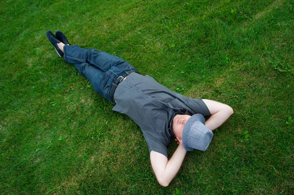 Muž ležící v oblasti na zelené trávě s kloboukem přes obličej — Stock fotografie