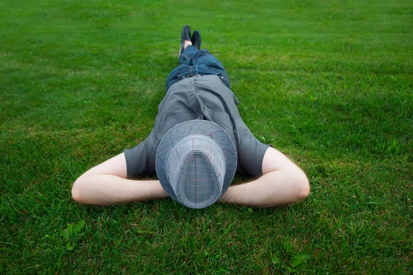 Homem deitado em um campo na grama verde com o chapéu sobre o rosto — Fotografia de Stock