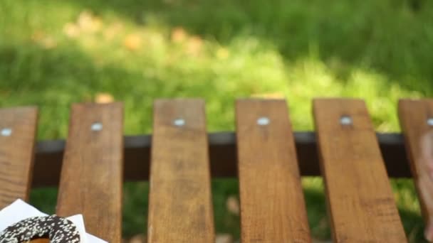 Красивая женщина сидит на скамейке в парке и ест кекс и латте — стоковое видео