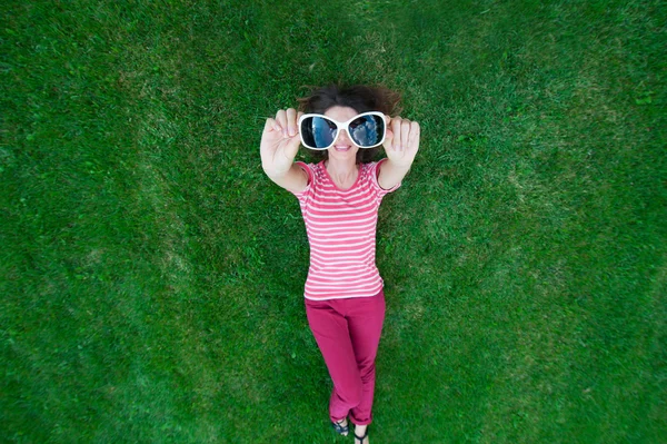 Schöne Frau liegt auf dem Gras und hält eine Brille in der Hand — Stockfoto