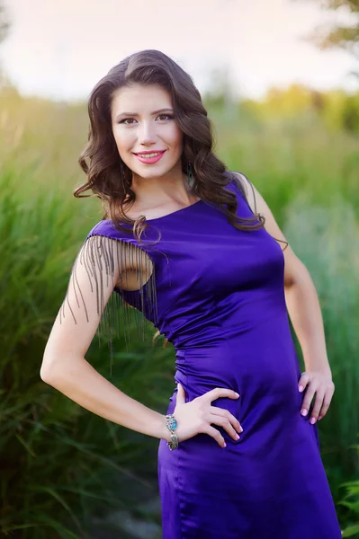 草原の上を歩いて薄紫色のドレスで美しい女性 — ストック写真