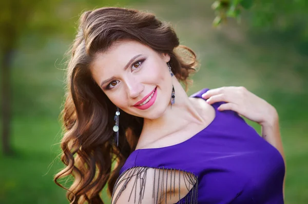 Young pretty women with long windy hair in elegant violet dresses standing on green grass — Stock Photo, Image